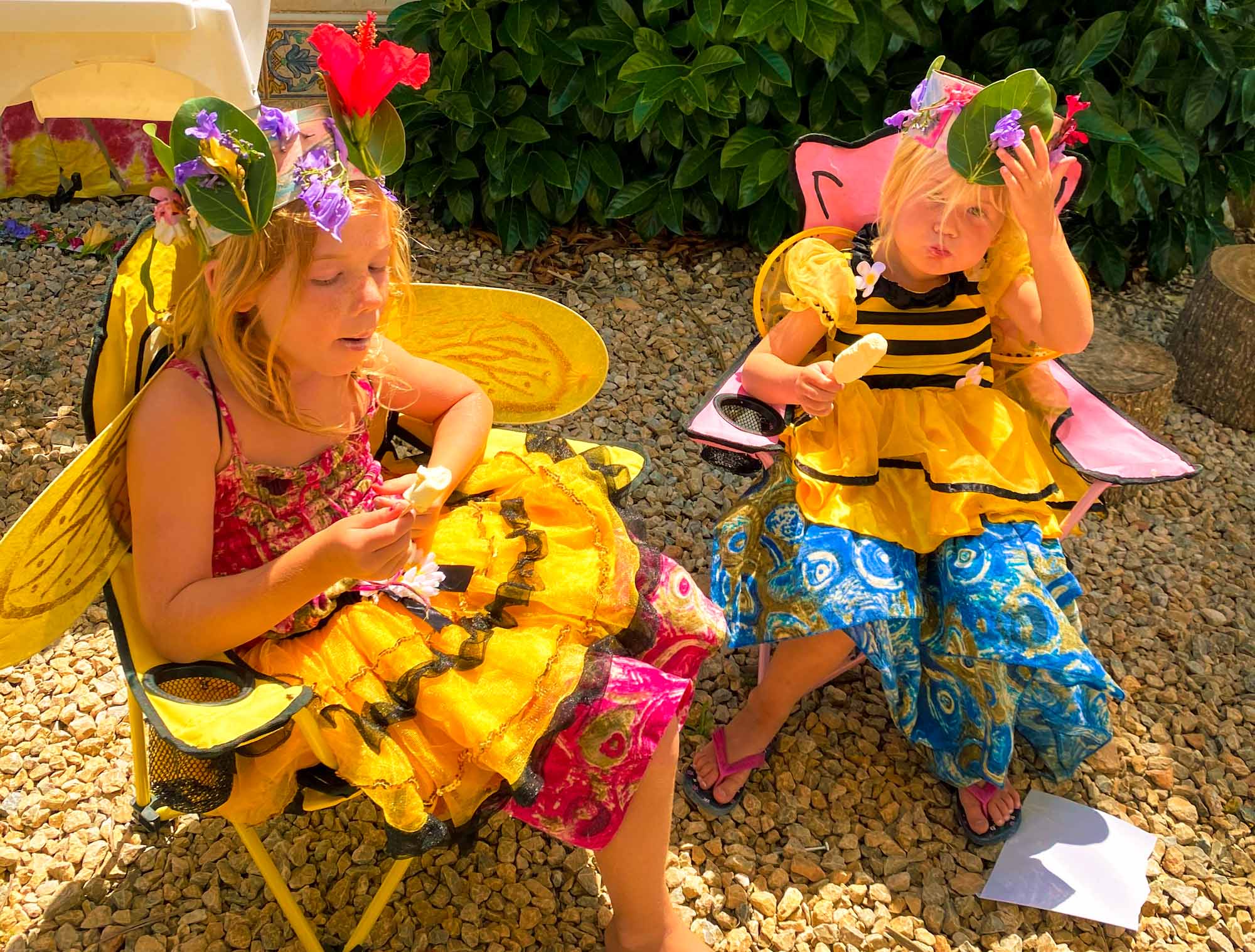 2 young girls sat wearing bee costumes and homemade flower crowns