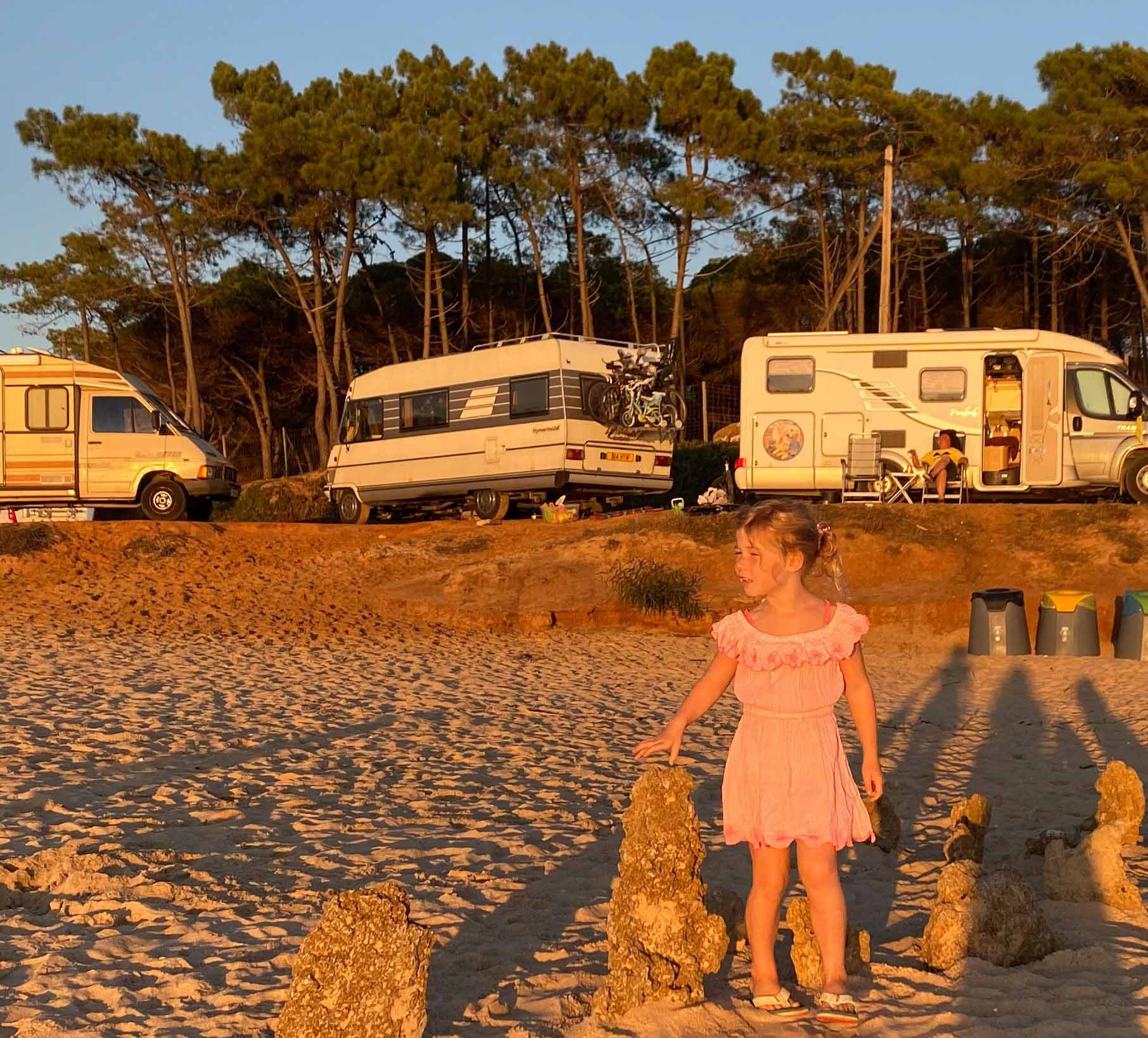 Girl stood on a sandy beach with motorhomes parked behind