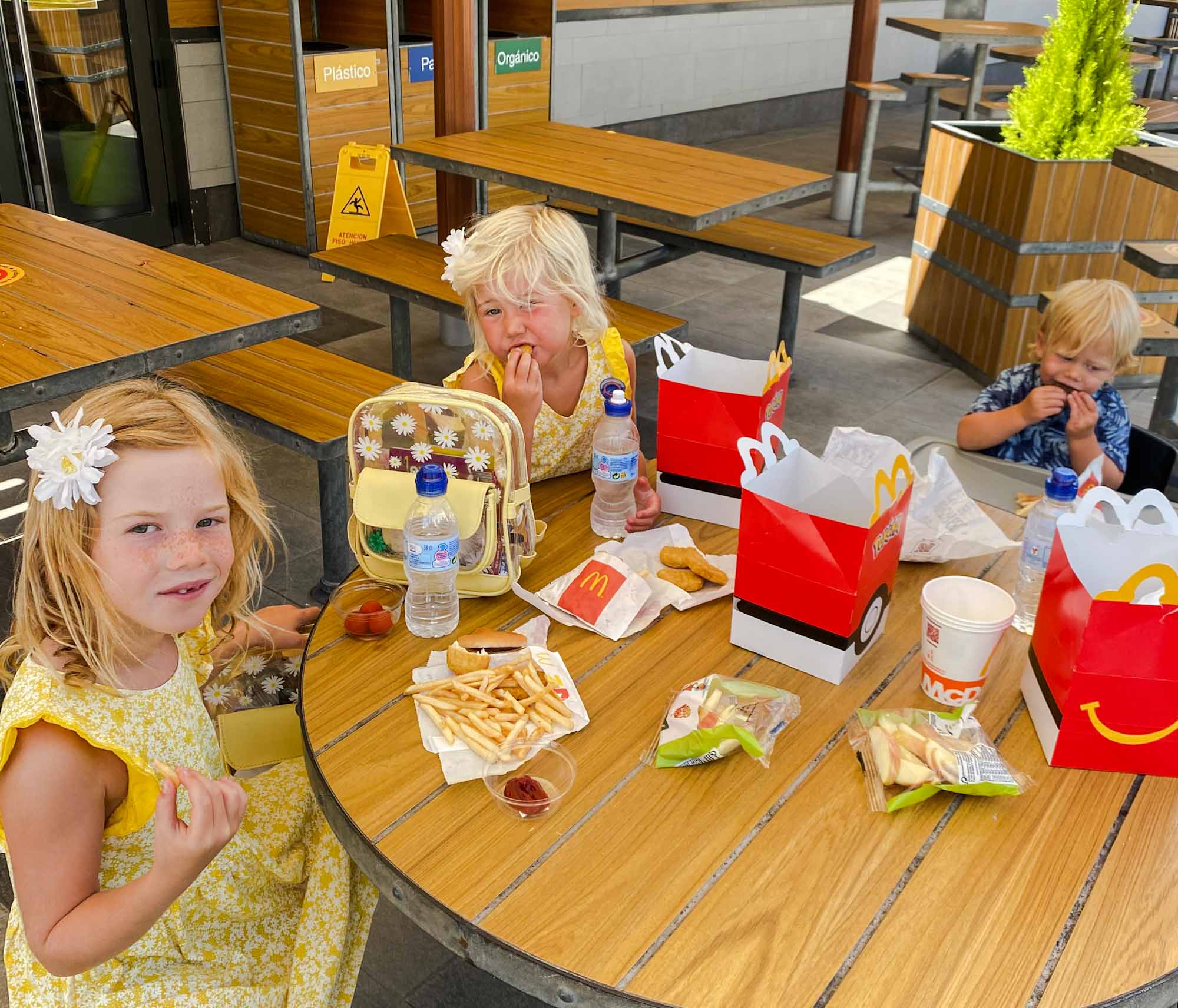3 young children sat an outside table eating McDonald's food