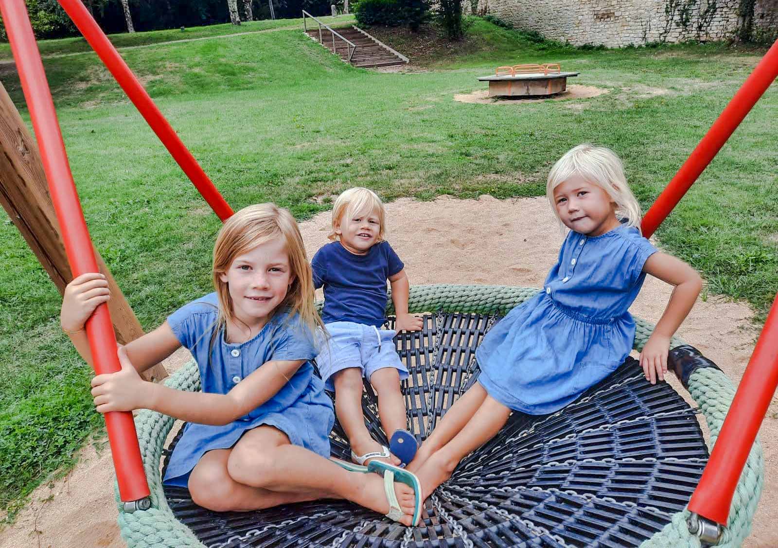 3 children sat on a circular group swing in a playground
