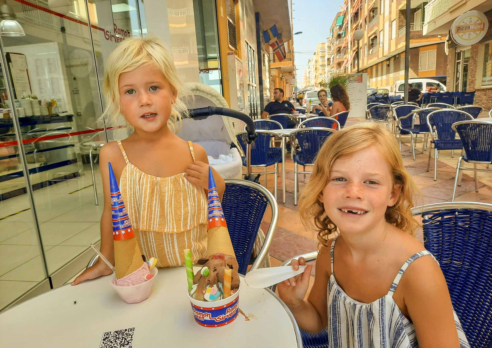 2 young girls eating large ice creams at an outdoor table