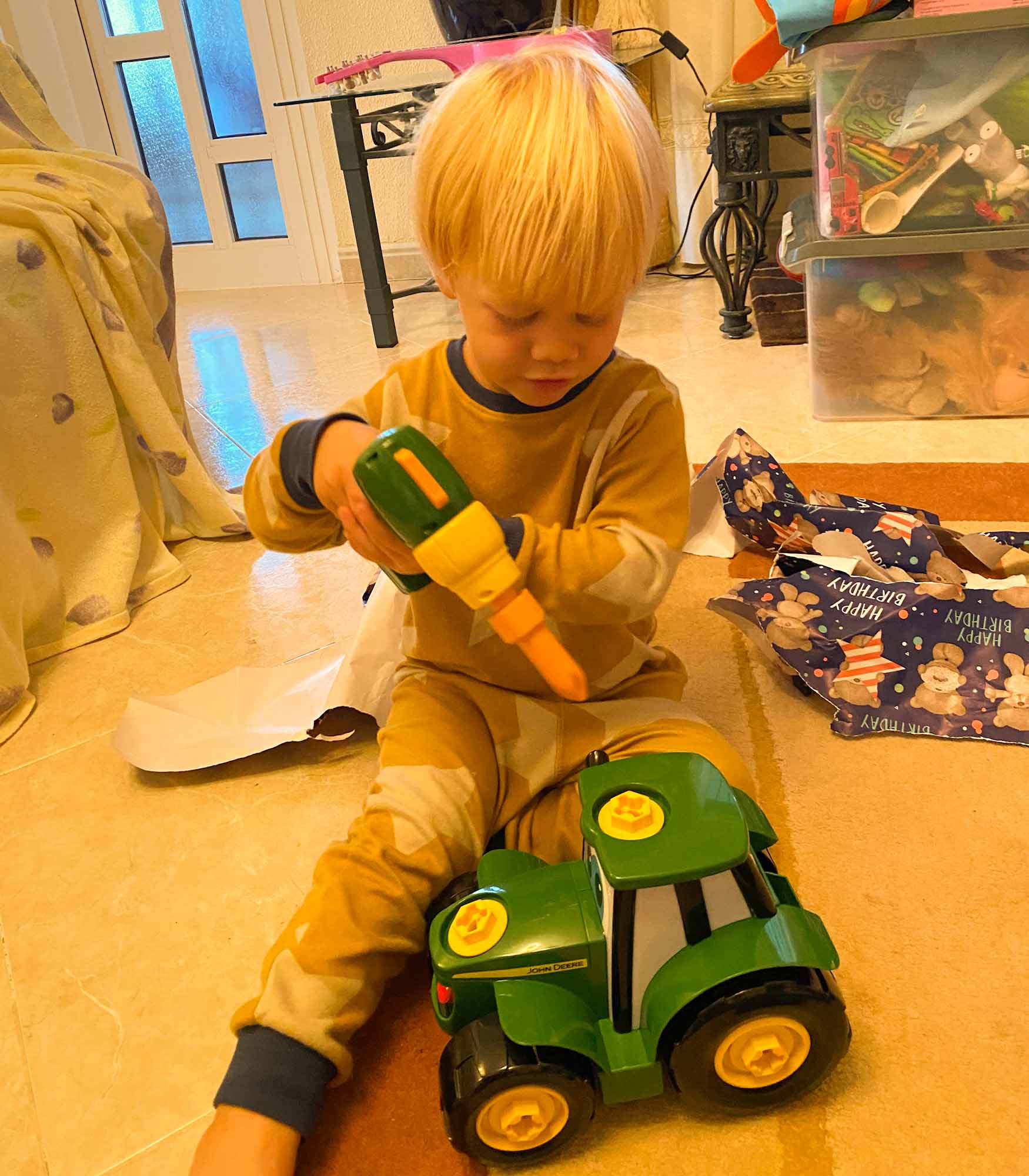 Young boy playing with a toy drill and tractor with ripped birthday wrapping paper behind