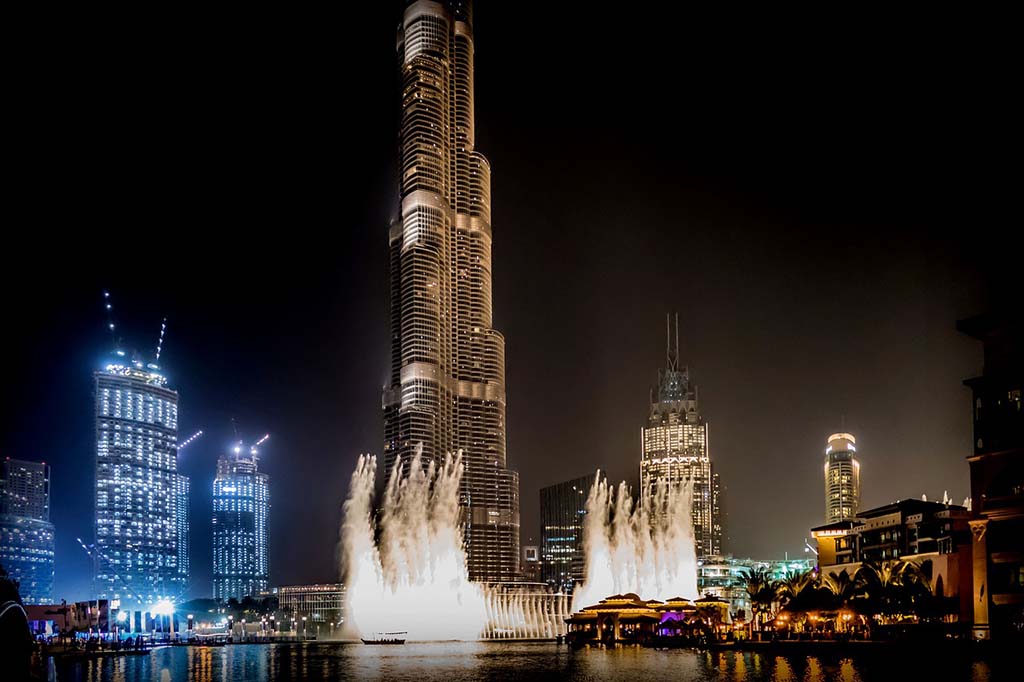An illuminated fountain show at night, in front of Dubai skyscrapers