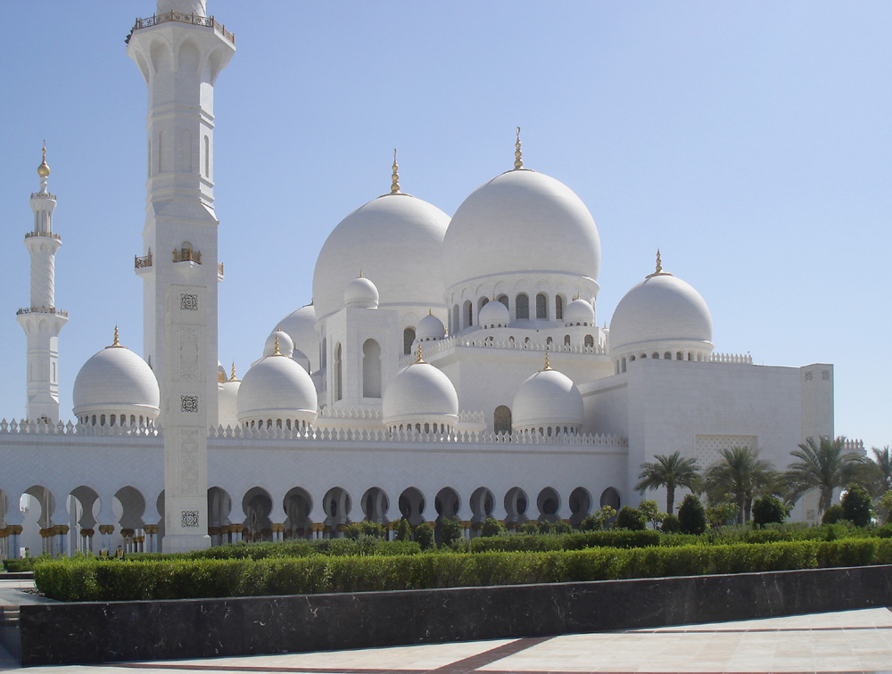 Exterior view of the white-washed Abu Dhabi Grand Mosque, complete with multiple-domed ceiling and minarets.