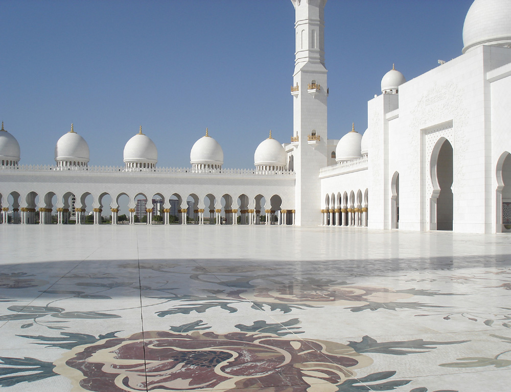 Looking across a marble-floored outdoor courtyard at a white painted mosque