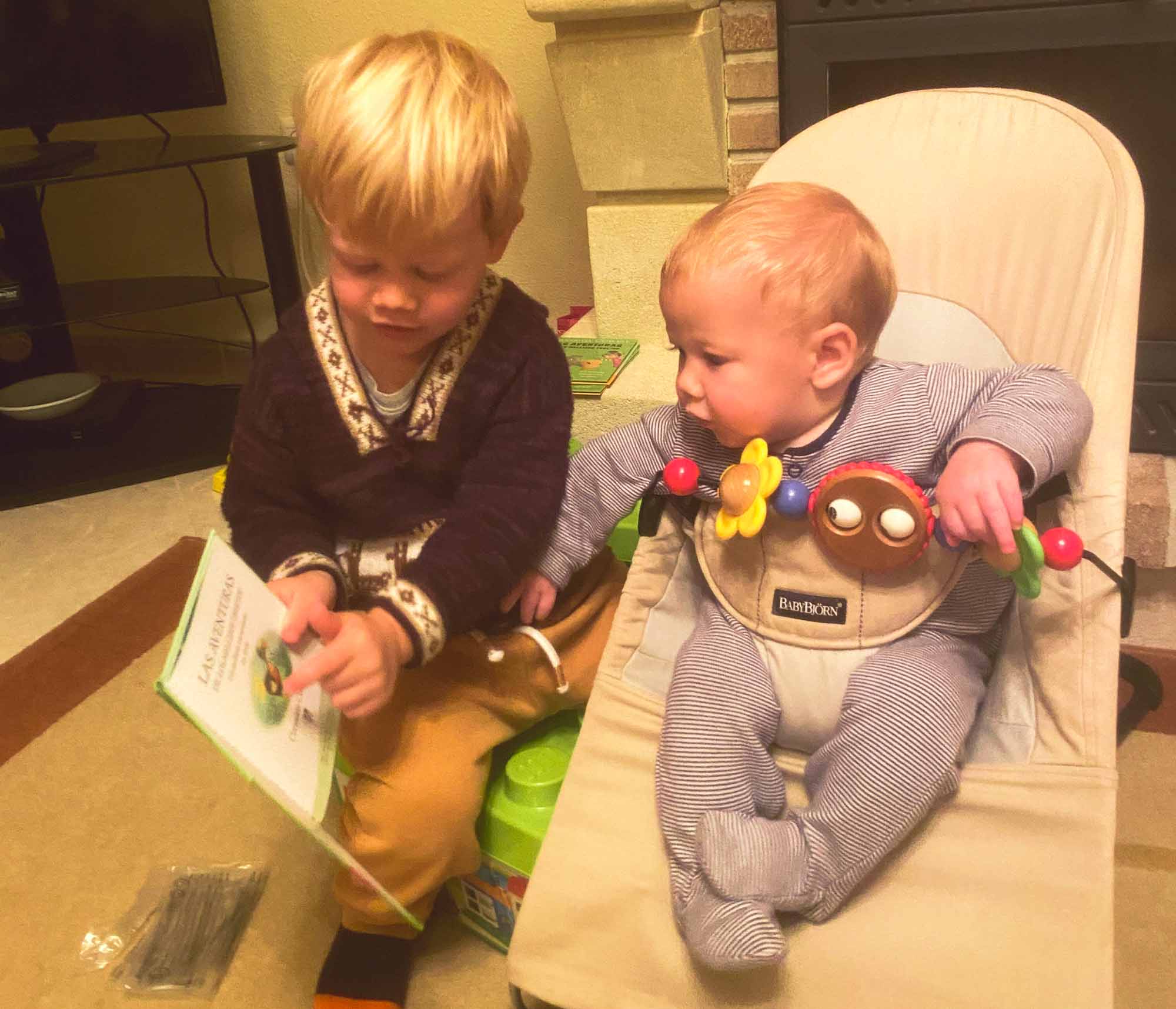Young boy showing a book to his baby brother sat in a bouncy chair