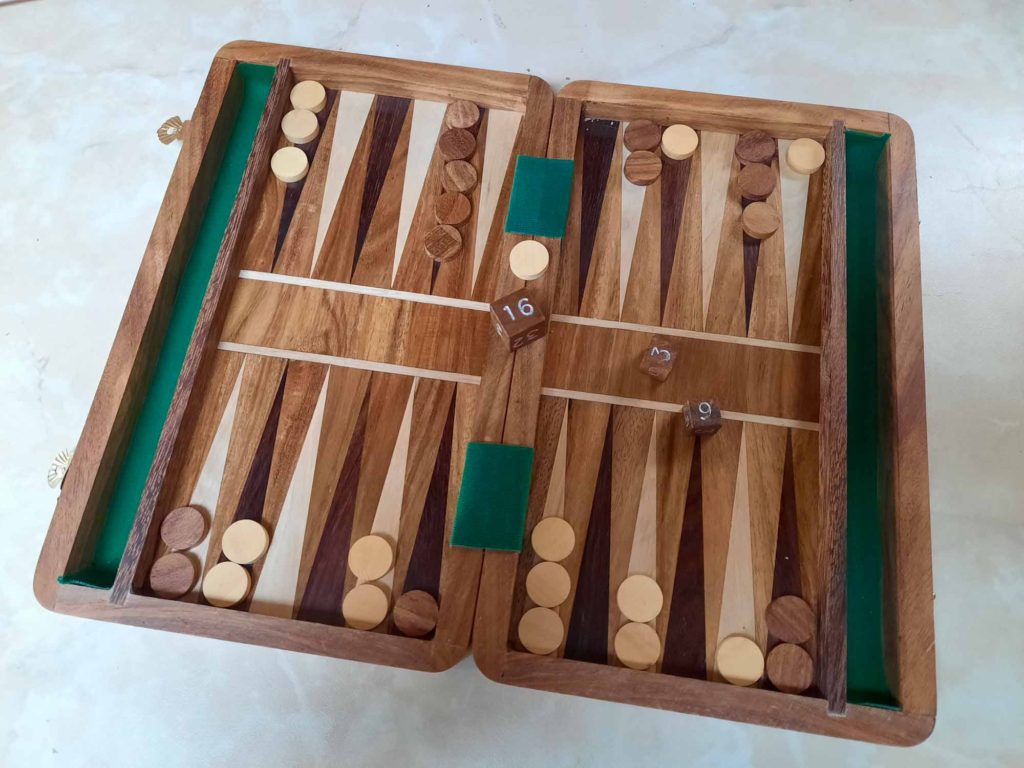 A wooden backgammon set, open on a table and mid-game