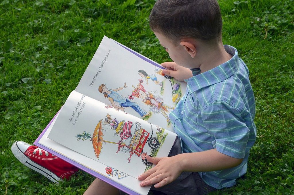 A boy sat on the grass reading a book with colourful pictures inside