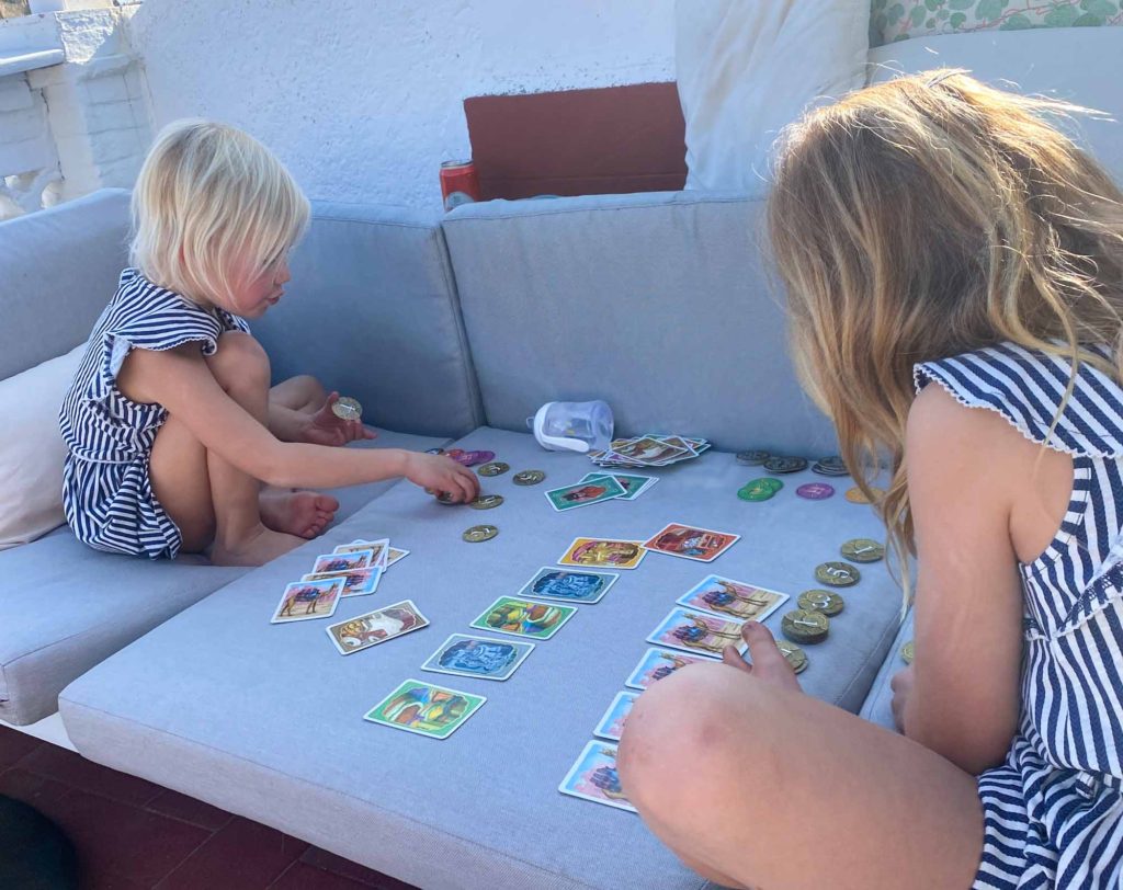 2 young girls sat on an outdoor sofa, playing the card game 'Jaipur'
