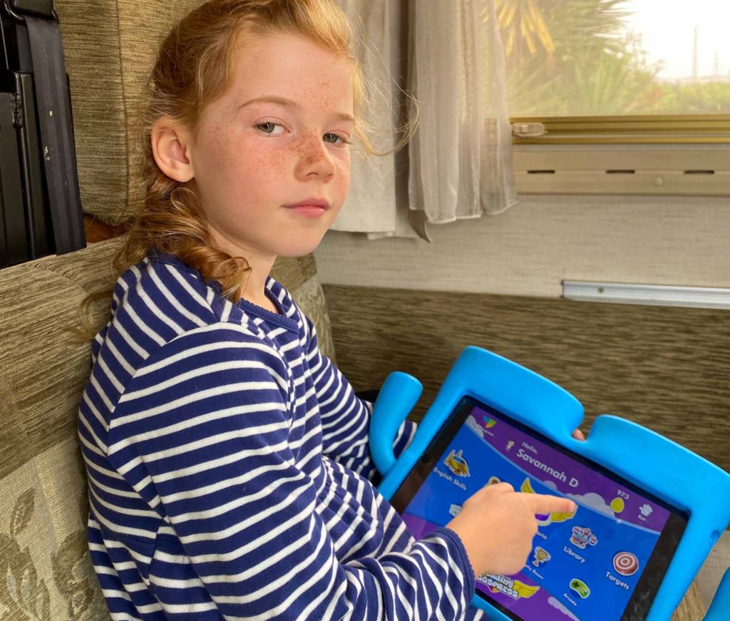 A girl sat in a campervan, using an iPad to play the 'Reading Eggs' learning app