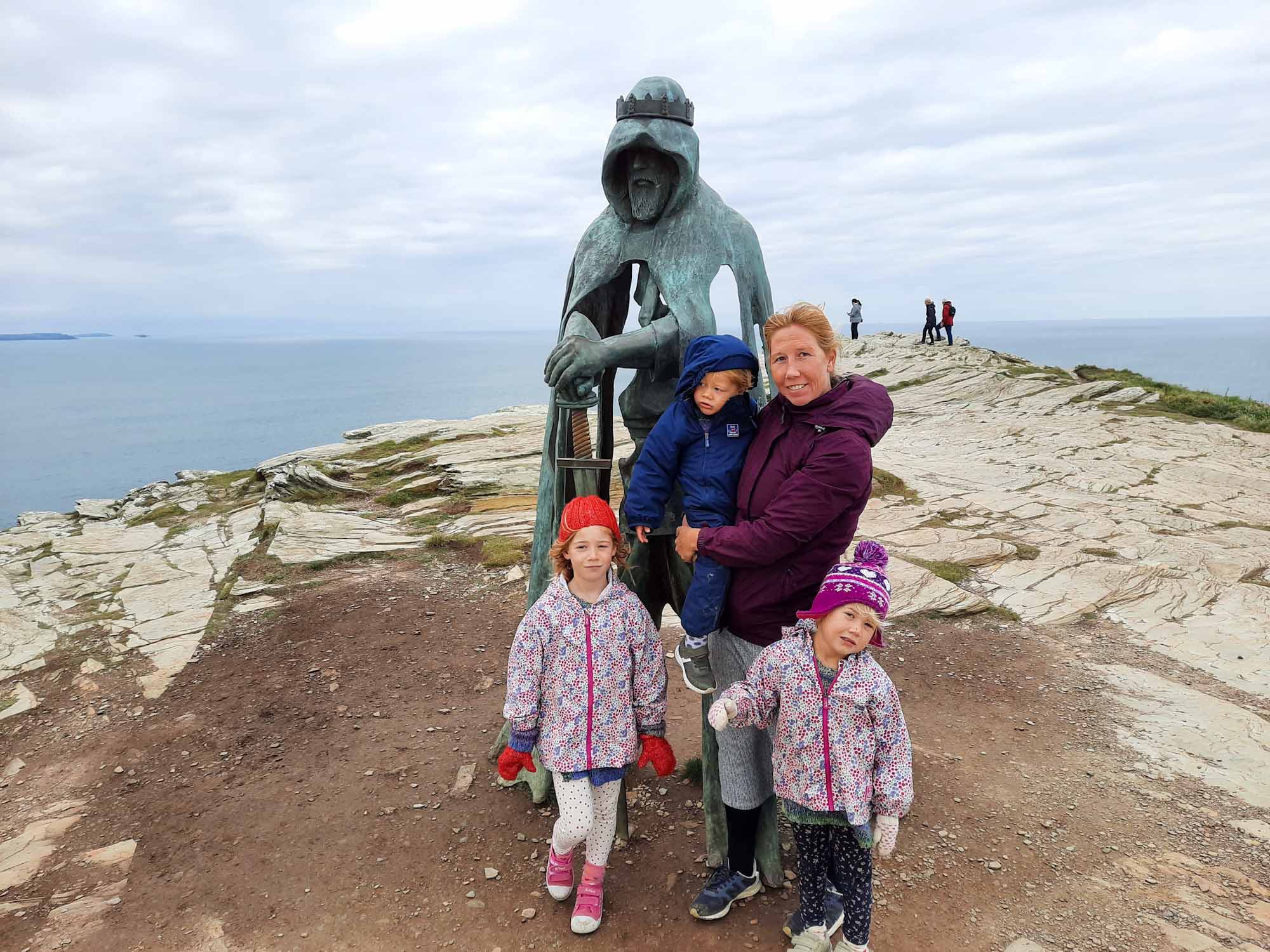A family stood on a clifftop with a metal sculpture depicting King Arthur