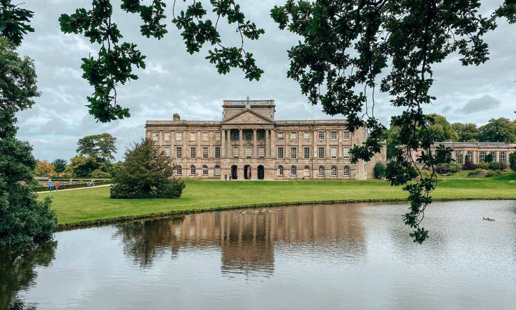 View across a lake of a grand, manor house, with columned frontage