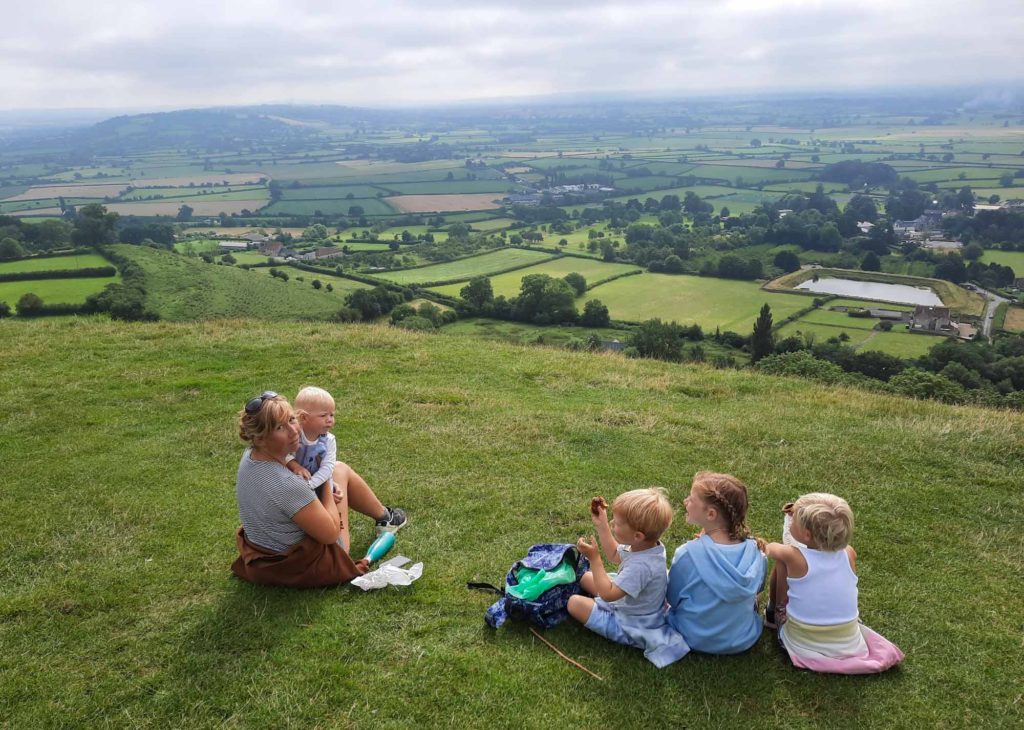 A family with 4 small children, sat at a countryside hilltop viewpoint