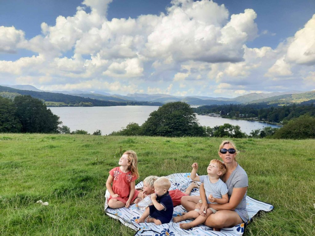 Family with small children eating a picnic on a rug, with lake views behind