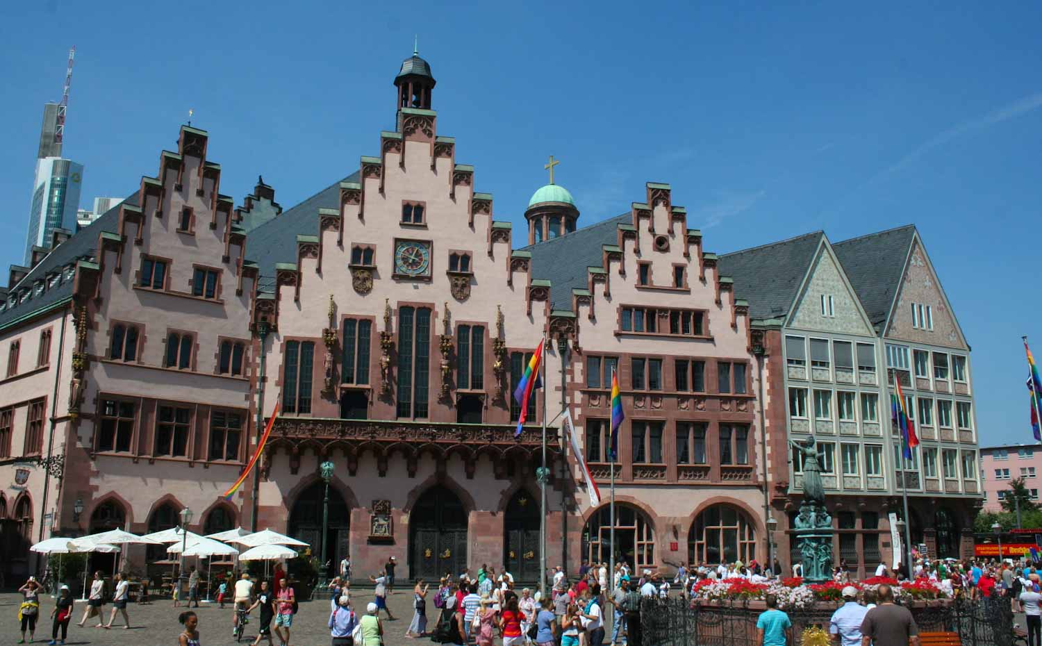 Large gabled building built in a German style, with busy pedestrian square in front