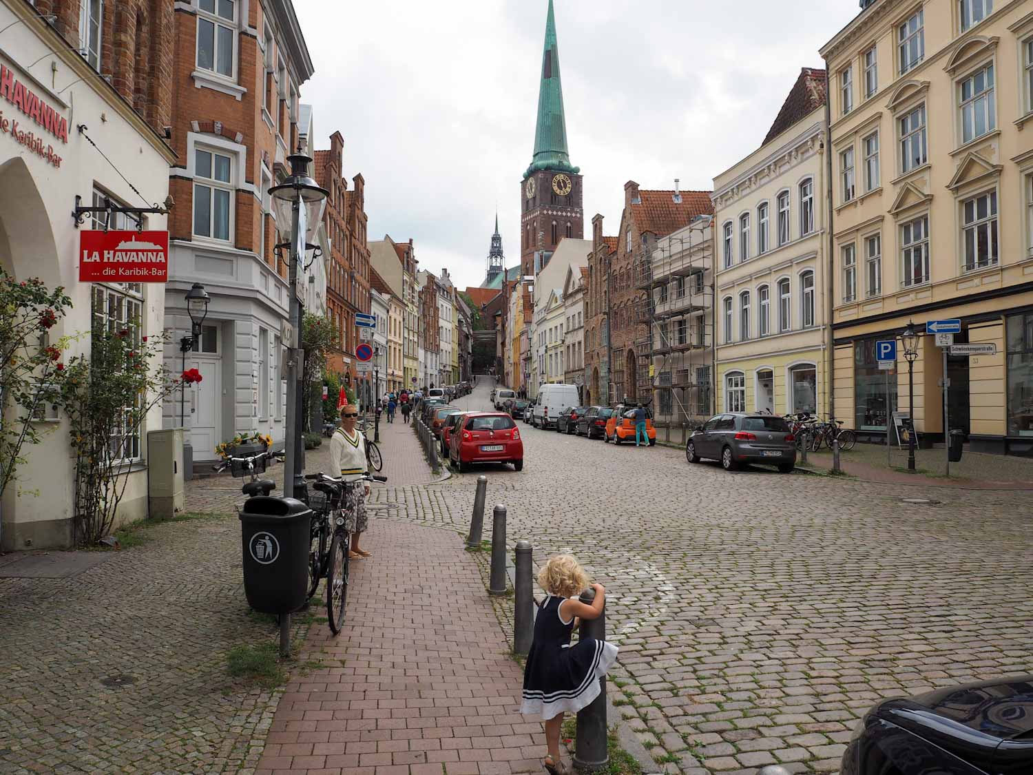 Small girl climbing on a bollard on a cobbled main street through a town
