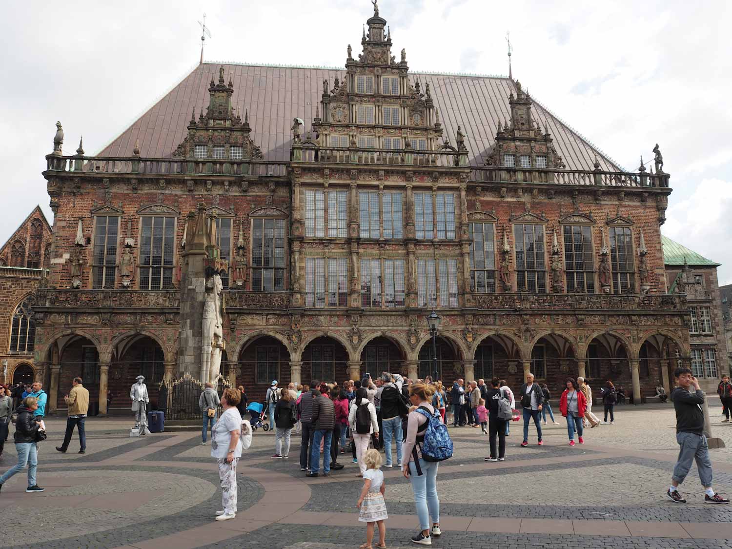 Crowds of people gathered outside a large, intricate, German town hall building