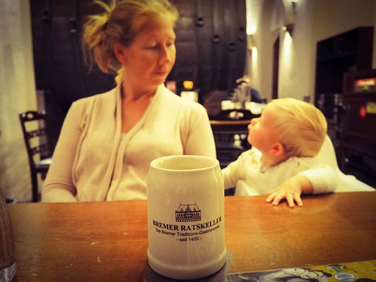 A pottery cup on a table with mother and baby behind, in a German beer hall
