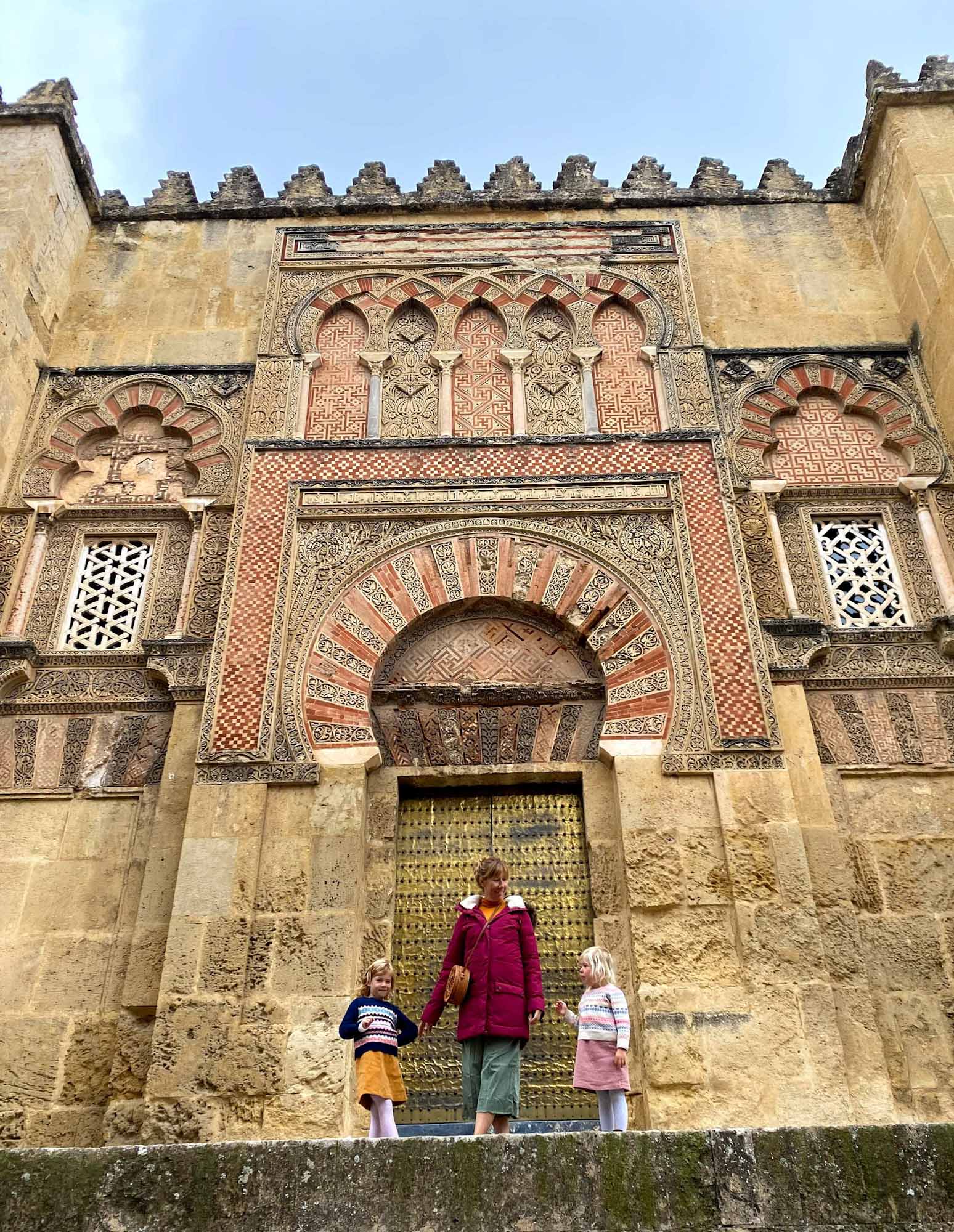 Mother with 2 daughters stood in front of a decorative, Moorish-design stone building