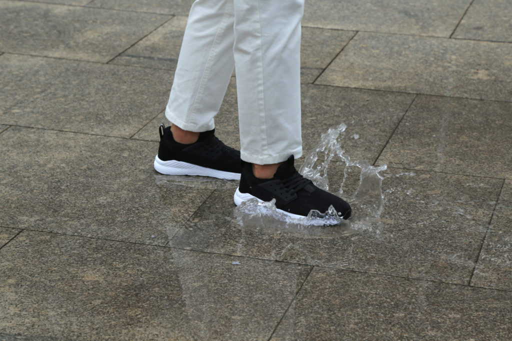 Black Loom Footwear trainers splashing in a puddle of water