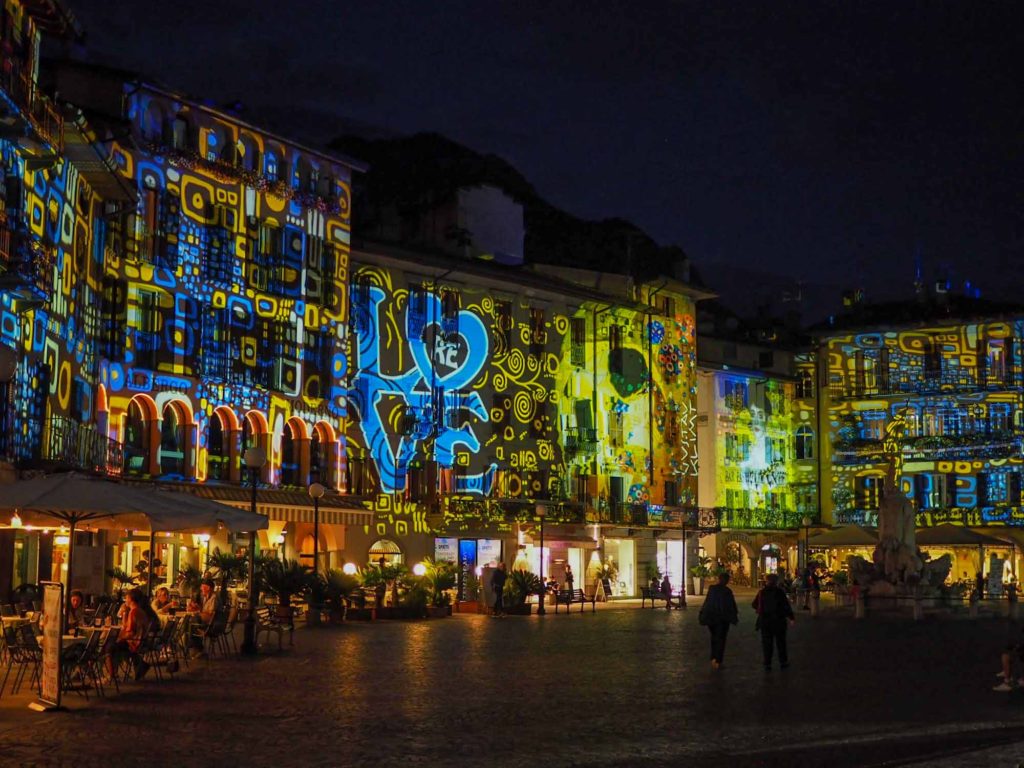 Large projected light display of colourful patterns and art onto stone building facades