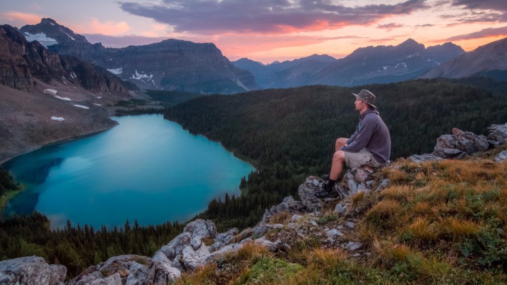 Man sitting alone overlooking a moutain lake at sunset