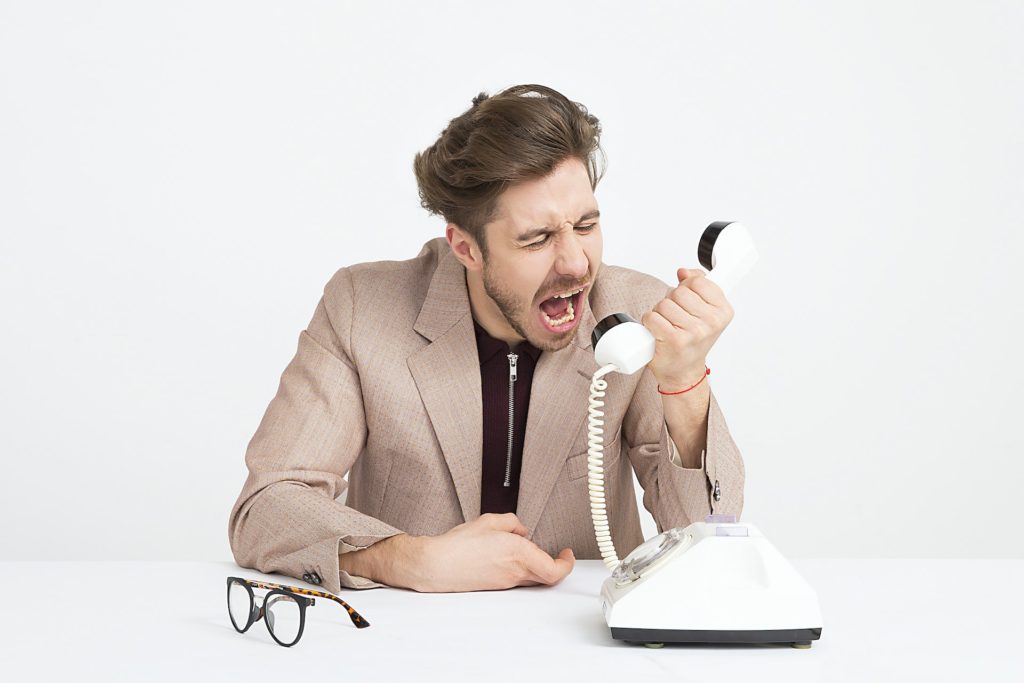 Man sat at a desk angrily shouting into a telephone